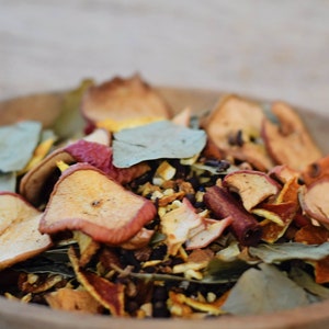 May include: A wooden bowl filled with dried fruit and spices, including apple slices, orange peel, cinnamon sticks, and bay leaves.