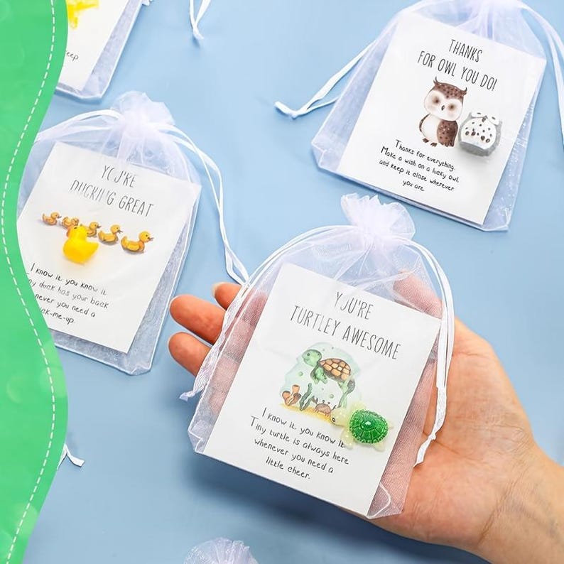 Pode incluir: Pequenas sacolas de organza brancas contendo cart&otilde;es com mensagens tem&aacute;ticas de animais e amuletos. Um cart&atilde;o diz "You're DUCKING GREAT" com amuletos de pato. Outro diz "Thanks for OWL YOU DO!" com uma coruja.