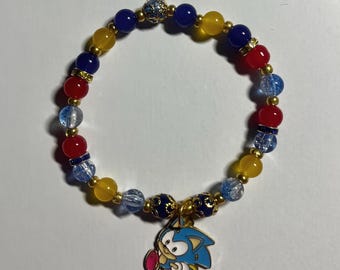 May include: A beaded bracelet featuring blue, yellow, and red beads, with gold-colored accents. A charm of the Sonic the Hedgehog character is attached. The bracelet is designed with a playful and colorful aesthetic.