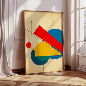 May include: Abstract art print featuring geometric shapes in red, yellow, blue, and black against a cream background. The artwork is framed in a gold-colored frame and leans against a white wall. The print includes a red rectangle, circles, and lines.