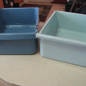 May include: Two enamelware rectangular baking dishes, one blue and one light blue, sitting on a white countertop.