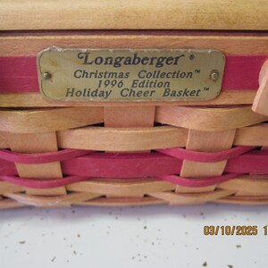 Pu&ograve; includere: Un cesto intrecciato con un design rosso e beige. Il cesto ha un'etichetta metallica che recita "Longaberger Christmas Collection 1996 Edition Holiday Cheer Basket."