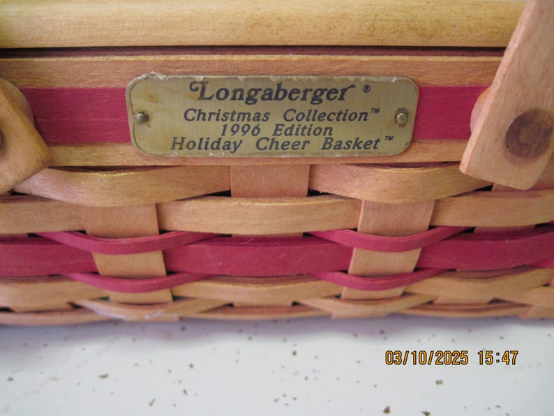 Pu&ograve; includere: Un cesto intrecciato con un design rosso e beige. Il cesto ha un'etichetta metallica che recita "Longaberger Christmas Collection 1996 Edition Holiday Cheer Basket."
