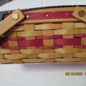 Pu&ograve; includere: Cesto intrecciato con manico. Il cesto presenta un colore legno naturale con accenti rossi intrecciati. Il manico &egrave; in legno e fissato con rivetti color rame. La fodera interna &egrave; verde con un motivo rosso e oro.