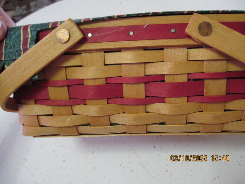 Pu&ograve; includere: Cesto intrecciato con manico. Il cesto presenta un colore legno naturale con accenti rossi intrecciati. Il manico &egrave; in legno e fissato con rivetti color rame. La fodera interna &egrave; verde con un motivo rosso e oro.