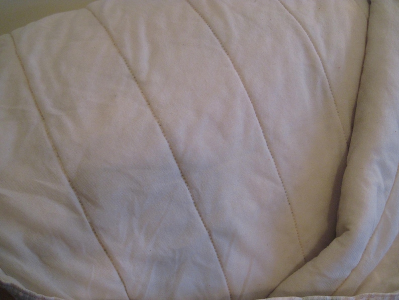 May include: Close-up of a cream-colored, quilted fabric. The fabric has a soft, textured appearance with diagonal stitching creating a series of parallel lines. The overall look is simple and neutral, suitable for bedding or upholstery.
