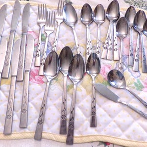 May include: A collection of vintage silverware, including knives, forks, and spoons, arranged on a floral patterned quilted placemat. The silverware has a decorative floral design on the handles. The image showcases a complete set of dining utensils.