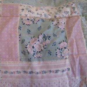 May include: Close-up of a patchwork quilt with floral and geometric patterns. The quilt features squares of light pink, pale green, and white fabric. Some squares have floral prints, while others have small dot patterns. The quilt is a mix of soft colors and textures.
