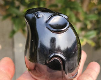May include: A glossy black figurine of a mouse, with rounded features and a smooth, polished surface. The mouse has large ears and a curved tail, and is held in a person's hand.
