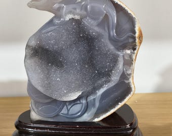 May include: A gray agate sculpture of a mouse perched atop a geode, mounted on a dark wooden base. The geode has a crystalline interior and a smooth, polished exterior. The sculpture is a unique decorative item.
