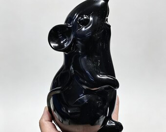 May include: A glossy black sculpture of a mouse, with a rounded body, large ears, and a long tail. The mouse is depicted in a seated position, with its mouth open. The sculpture is held in a hand against a white background.