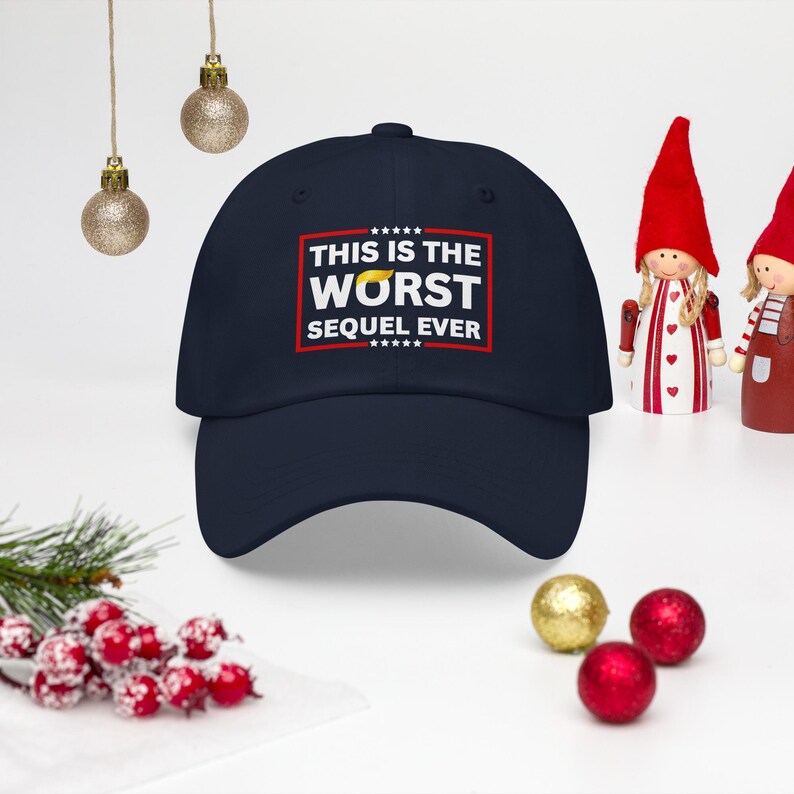 Pu&ograve; includere: Un cappellino da baseball blu navy con la scritta "THIS IS THE WORST SEQUEL EVER" in bianco e rosso. Il cappellino ha una visiera curva e una corona strutturata. L'immagine include decorazioni natalizie.