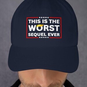 Pu&ograve; includere: Cappellino da baseball blu navy con la scritta "THIS IS THE WORST SEQUEL EVER" in lettere bianche all'interno di un rettangolo rosso. La parola "WORST" ha un disegno giallo a forma di capelli sopra. Il cappellino ha una visiera curva.