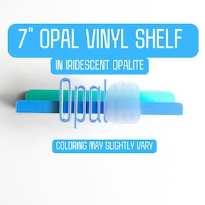 May include: A 7-inch opal vinyl shelf in iridescent opalite. The shelf is blue with a light blue, green, and blue accent. The text on the image reads "Coloring may slightly vary."