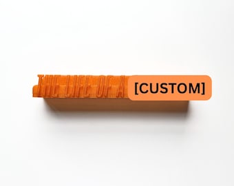 Könnte beinhalten: Ein orangefarbener rechteckiger Stempel mit dem Text "HELLELUJA" auf der Oberseite. Ein rechteckiger orangefarbener Aufkleber mit dem Wort "[CUSTOM]" ist an der Seite angebracht. Der Stempel befindet sich vor einem weißen Hintergrund.