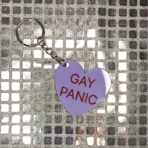 May include: A purple heart-shaped keychain with a silver chain and the text "GAY PANIC" in red letters.