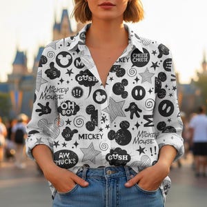 Puede incluir: Camisa blanca con botones con un estampado en blanco y negro de Mickey Mouse. El diseño incluye siluetas de Mickey Mouse, estrellas, bocadillos de texto con palabras como "Gush" y "Oh Boy", y las palabras "Mickey Mouse" y "Cheese Key".