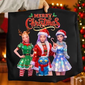 Puede incluir: Sudadera negra con un gráfico festivo. El diseño presenta a tres mujeres animadas con atuendos navideños, un gato azul y las palabras "Merry Christmas" en rojo y dorado. Las mujeres llevan gorros de Papá Noel y vestidos.