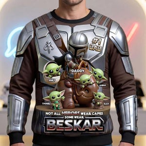 Puede incluir: Sudadera marr&oacute;n con un dise&ntilde;o inspirado en The Mandalorian, con Grogu y el texto "#1 DAD". El dise&ntilde;o incluye los nombres "Emily", "Daniel", "Anna" y "Alex". Tambi&eacute;n est&aacute; presente el texto "NOT ALL HEROES WEAR CAPES SOME WEAR BESKAR".