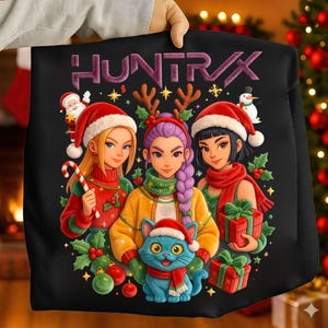 May include: Black sweatshirt featuring a festive illustration with three women wearing Santa hats and scarves, surrounded by Christmas decorations. A blue cat in a Santa hat is in the center. The word "HUNTR/X" is at the top.