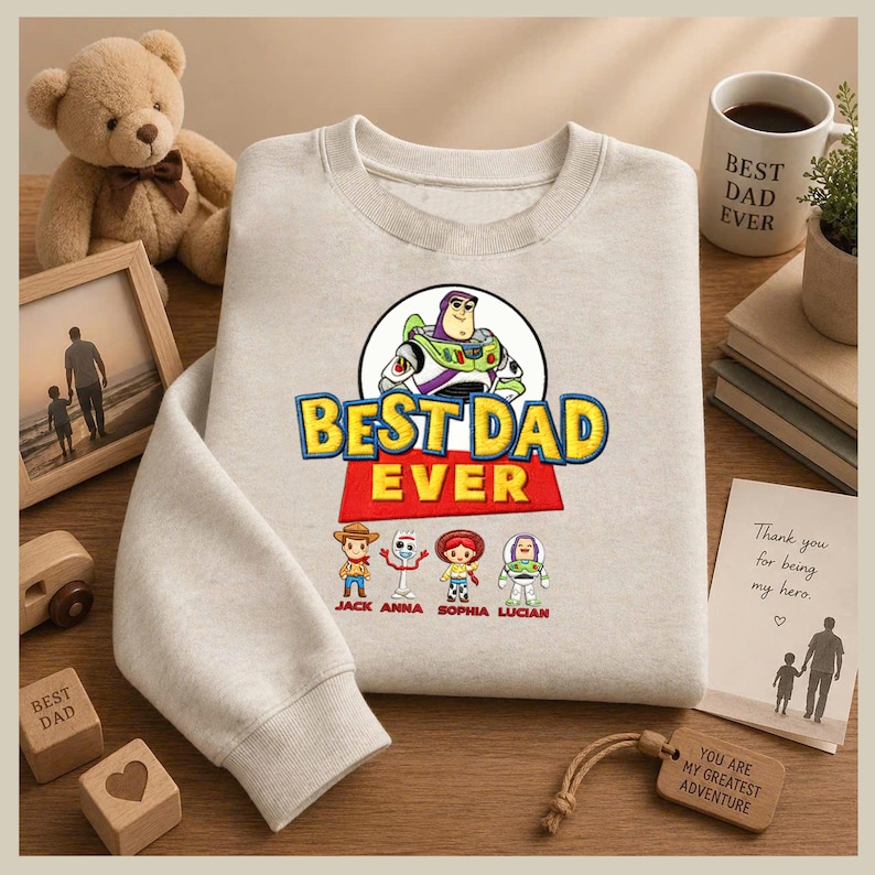 May include: A light gray sweatshirt with the text "BEST DAD EVER" in yellow and red, featuring a Buzz Lightyear graphic and cartoon characters. Below the text are the names "JACK ANNA SOPHIA LUCIAN".
