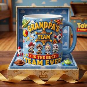 May include: A blue ceramic mug with the text "GRANDPA'S TEAM IS THE BEST TEAM EVER" and Toy Story character illustrations. The mug is in a gift box with a gold ribbon and a small toy cowboy hat and alien figurine.