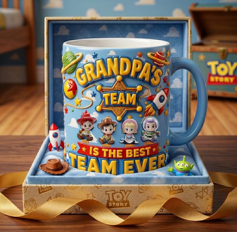 May include: A blue ceramic mug with the text "GRANDPA'S TEAM IS THE BEST TEAM EVER" and Toy Story character illustrations. The mug is in a gift box with a gold ribbon and a small toy cowboy hat and alien figurine.
