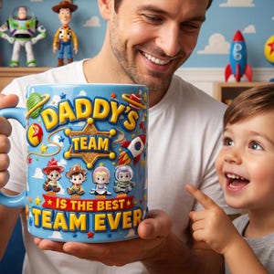 May include: A blue ceramic mug with the text "DADDY'S TEAM IS THE BEST TEAM EVER" and cartoon character illustrations. The mug has a blue handle and is held by a person. Toy Story figures are visible in the background.