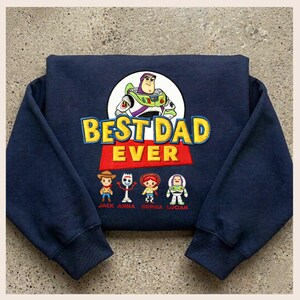 May include: Navy blue sweatshirt featuring a graphic of Buzz Lightyear and the phrase "BEST DAD EVER" in yellow and red. Below the text are cartoon character illustrations. The names Jack, Anna, Sophia, and Lucian are printed below the characters.