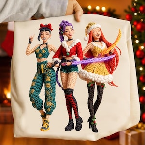 Puede incluir: Un cojín crema con una colorida ilustración de tres mujeres estilizadas con trajes festivos. Las mujeres están representadas con ropa de ganchillo, una de ellas con un gorro de Papá Noel. El cojín lo sostiene una persona.
