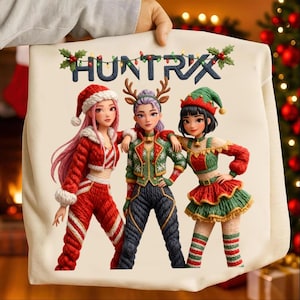 Puede incluir: Bolso tote color crema con la palabra "HUNTRIX" bordada en la parte superior. La imagen muestra tres personajes de dibujos animados con atuendos navideños. Llevan trajes rojos, verdes y blancos con sombreros y accesorios festivos.
