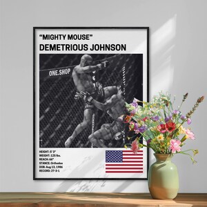 The image is a framed poster featuring a black and white photograph of Demetrios Johnson, a professional mixed martial artist, in the ring. The poster also includes text providing information about Demetrios Johnson, such as his height, weight, reach, and record. In the foreground, there is a vase with colorful flowers, adding a decorative element to the scene.