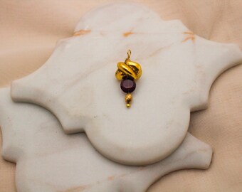 May include: Gold pendant with a knotted design and a dark red gemstone.