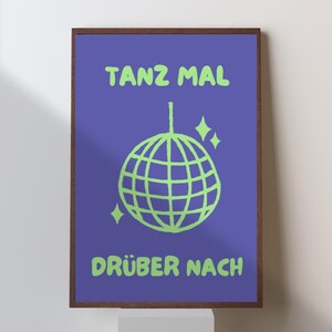 Könnte beinhalten: Ein gerahmtes Poster mit einem violetten Hintergrund und grünem Text, der "TANZ MAL" und "DRÜBER NACH" lautet. Eine grüne Discokugel mit Glitzer befindet sich in der Mitte des Posters.