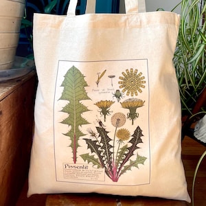 May include: A natural canvas tote bag displaying a botanical print of a dandelion plant. The illustration shows the plant's various parts, including leaves, flowers, and seed heads, with French text "Fleur et fruit grossie" and "Pissenlit".
