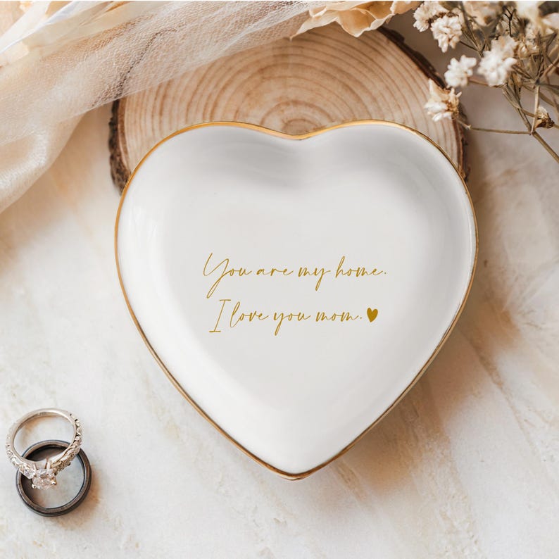May include: White heart-shaped trinket dish with a gold rim. The dish has the text "You are my home. I love you mom." written in gold lettering.