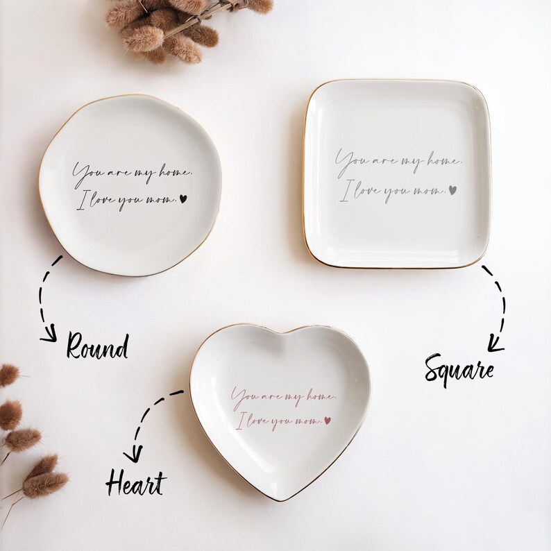 May include: Three ceramic trinket dishes in round, square, and heart shapes. Each dish has a gold rim and features the text "You are my home. I love you mom." in black script with a small pink heart.