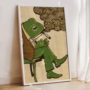 May include: Framed art print featuring a green frog in a suit, smoking a cigarette. The frog is seated on a chair, with a brown vest and green pants. The background is a neutral beige with a swirl of smoke.