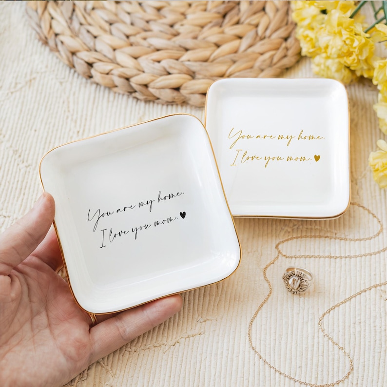 May include: Two white ceramic trinket dishes with gold trim. Each dish has the text "You are my home. I love you mom." written in black script with a small black heart.