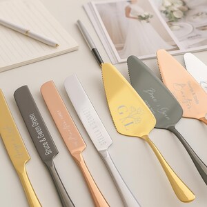 May include: An assortment of personalized cake servers in gold, silver, and rose gold. Each server has a unique design and engraved names. A notebook and pen are in the background, along with a wedding photo.