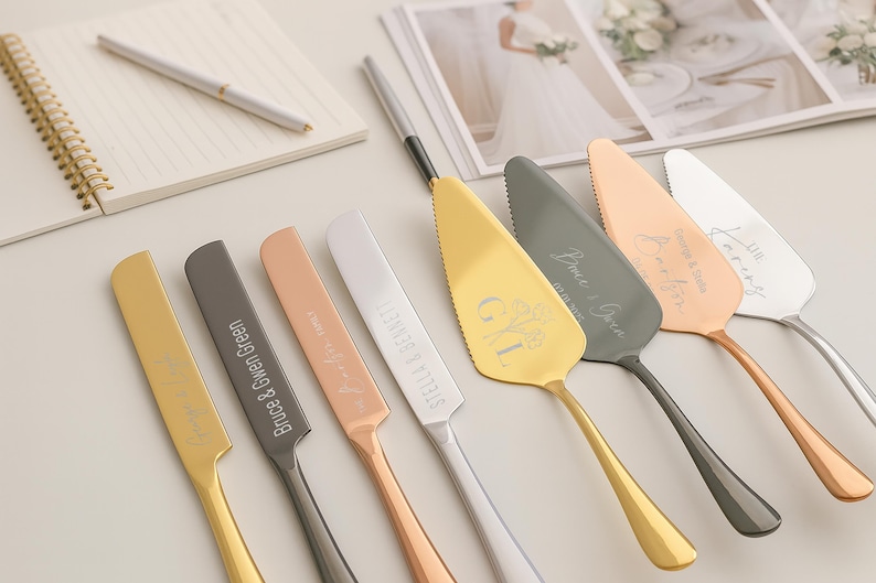 May include: An assortment of personalized cake servers in gold, silver, and rose gold. Each server has a unique design and engraved names. A notebook and pen are in the background, along with a wedding photo.