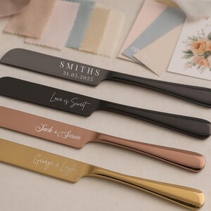 May include: Four personalized cake knives in black, rose gold, and gold tones, with engraved text. The knives are arranged on a light surface, with wedding-themed stationery and fabric swatches in the background. The text includes names and dates.