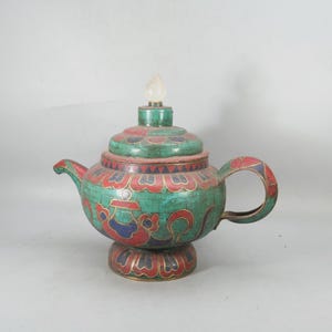 May include: A teapot featuring a turquoise-colored mosaic surface with inlaid red and blue patterns, a curved handle, a short spout, and a lid topped with a clear, translucent finial. The base is circular and decorated with matching colors.