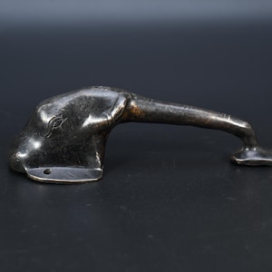 Peut inclure: Une poignée de porte en métal sombre en forme de tête d'animal avec un cou allongé. L'objet présente une finition lisse et patinée avec des trous de fixation visibles à la base et à l'extrémité du cou, montrant une construction en métal moulé.
