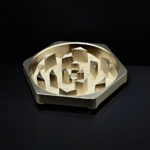 Pode incluir: Um moedor de ervas hexagonal dourado, com dentes triangulares afiados. O moedor tem uma c&acirc;mara central e uma superf&iacute;cie texturizada, projetada para moer de forma eficiente. O acabamento met&aacute;lico confere-lhe uma apar&ecirc;ncia elegante e moderna.
