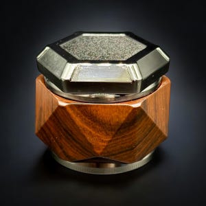 Pode incluir: Um moedor de madeira com um design geom&eacute;trico e um topo met&aacute;lico facetado. A madeira tem uma cor marrom-avermelhada rica, e o topo &eacute; prateado. O moedor foi projetado para ficar em uma superf&iacute;cie plana.