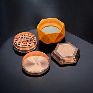 Pode incluir: Um moedor de ervas desmontado em cobre e madeira. O moedor &eacute; composto por v&aacute;rias partes, incluindo uma parte superior com uma superf&iacute;cie de moagem estampada, uma parte inferior com um pequeno raspador de pl&aacute;stico e um recipiente hexagonal de madeira.