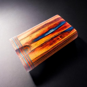 May include: A wooden box with a blue and orange wood grain pattern. The box has a small hole in the top and a blue, red, and white trim around the edges.