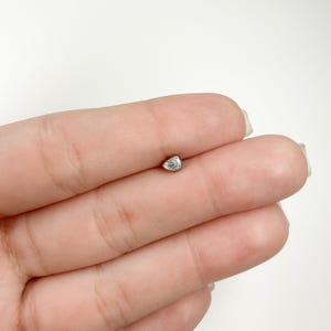 May include: A small, clear, teardrop-shaped gemstone set in a silver stud earring.