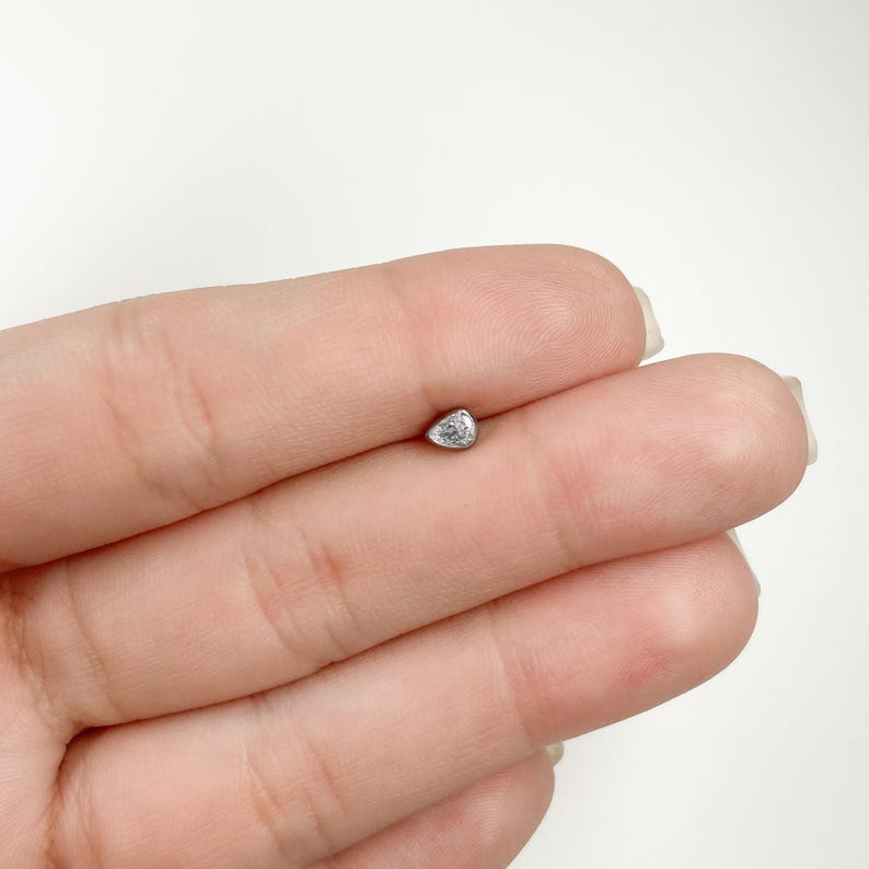May include: A small, clear, teardrop-shaped gemstone set in a silver stud earring.
